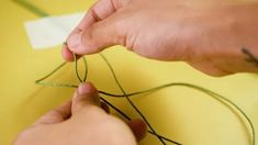 someone is working on something with green thread and scissors in their hands, while another person holds the string