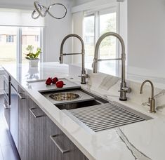 a white kitchen with marble counter tops and stainless steel faucet, sink, and window