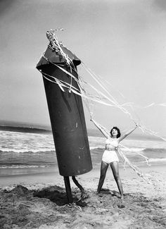 a woman in a bathing suit holding a kite on the beach next to an object