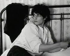 black and white photograph of a young man sitting on a bed