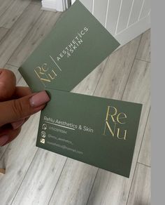 two business cards being held up in the air by someone's hand on a wood floor