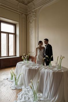 a bride and groom standing next to each other in front of a table with flowers on it