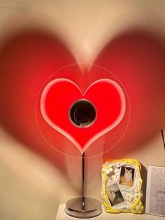 a red heart shaped lamp sitting on top of a table next to a photo frame