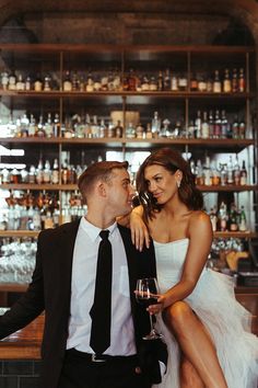 a man and woman sitting next to each other in front of a bar filled with liquor bottles