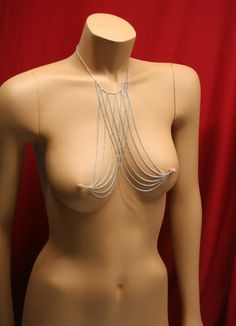 a female mannequin with silver chains on it's neck and chest, in front of a red background