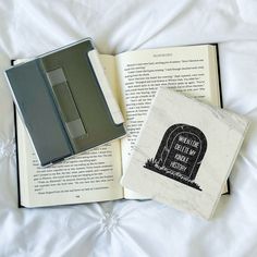 an open book sitting on top of a white bed next to a black and gray wallet