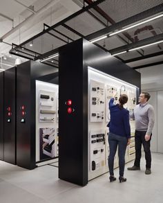 two people are looking at electronic equipment in a room with white walls and black floors