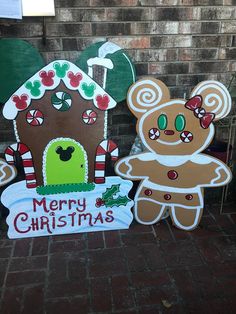 two cardboard christmas signs on the side of a brick building with a teddy bear and gingerbread house