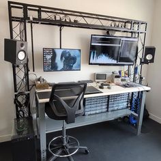 a computer desk with two monitors and speakers on the wall above it, along with other equipment