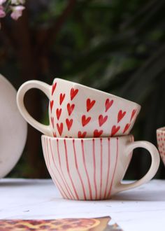 two cups with hearts painted on them are sitting next to each other near plates and flowers