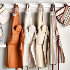 several aprons hanging from hooks on a wall next to other kitchen utensils