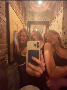 three women are taking a selfie in the mirror with their cell phone while standing next to each other