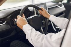 a man driving a car with his hands on the steering wheel while wearing a white shirt