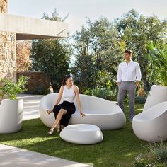 a man and woman standing next to a large white bath tub in the middle of grass