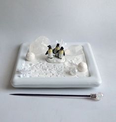 two small penguins sitting on top of a white plate next to an artist's paintbrush