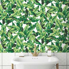 a white sink sitting under a green leafy wallpaper next to a bath tub