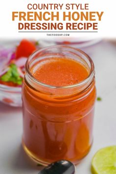 a jar filled with orange liquid next to a spoon and some sliced limes on the table