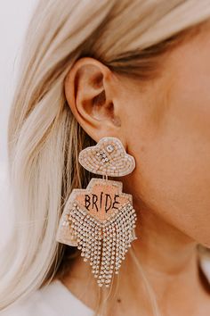 a woman wearing earrings with the word bride written on it and fringe tassels