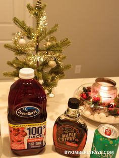 bottles of maple syrup and other holiday drinks on a table with a christmas tree in the background