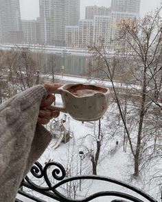 a person holding a cup in their hand while looking out over the snow covered park