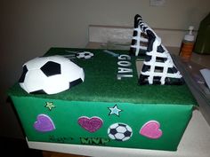 a cake shaped like a soccer ball and goalie's boot on top of a green box