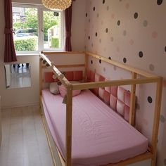 a small child's bed in a room with polka dot wallpaper and pink sheets