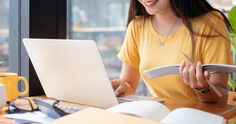 a woman sitting at a table with a laptop and papers in front of her smiling