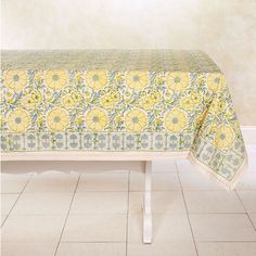 a yellow and green tablecloth on a white bench in front of a beige wall