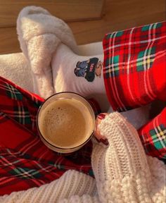 a person in red and green plaid pants holding a cup of hot chocolate on top of their feet