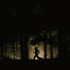 a man running through the woods at night with light shining on him and trees in the background