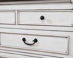 a white dresser with black handles and knobs