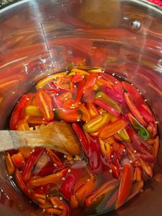 red and yellow peppers are being cooked in a pot with a wooden spoon on the side