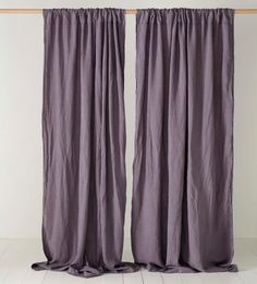 two purple curtains hanging on a wooden rail in front of a white wall and floor