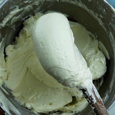 a metal bowl filled with white frosting and a wooden spoon sticking out of it