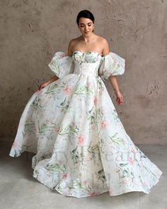 a woman in a white dress with flowers on it, standing against a concrete wall