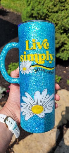 a hand holding a blue coffee mug with white daisies on it and the words live simply