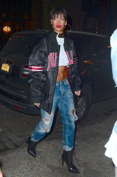 a woman in ripped jeans and a black jacket is standing next to a parked car