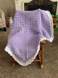 a purple crocheted blanket sitting on top of a wooden chair in front of a fireplace