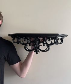 a man is holding up a shelf that has an ornate design on the top and bottom