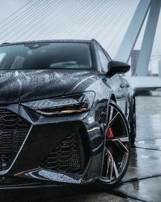 the front end of a black sports car on a wet street with a bridge in the background