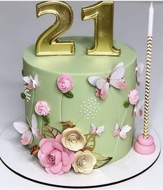 a green cake with pink flowers and gold number twenty on it's side, next to a lit candle