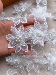 white flowers and pearls are being held by someone's hand on a piece of fabric