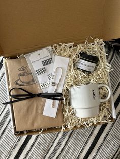 an open box containing coffee mugs, books and other items on a striped tablecloth