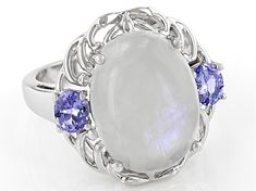 16x12mm Oval Cabochon Rainbow Moonstone With 0.68ctw Oval Tanzanite Rhodium Over Sterling Silver Ring. Measures Approximately 0.78"L x 0.63"W. Not sizeable. White Cabochon Moonstone Ring In Fine Jewelry Style, Fine Jewelry White Cabochon Moonstone Ring, White Cabochon Moonstone Ring Fine Jewelry, White Oval Cabochon Moonstone Ring, White Moonstone Ring With Accent Stones, White Oval Cabochon Moonstone Ring With Gemstone, Oval Moonstone Ring In White Gold, White Moonstone Ring With Oval Cabochon, Fine Jewelry Oval Multi-stone Moonstone Ring