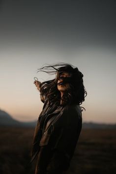 a woman standing in the middle of a field with her hair blowing in the wind