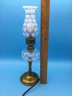 a glass lamp sitting on top of a table next to a tall ruler with a blue background