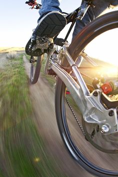 a person riding a bike on a dirt road with the sun shining through the grass