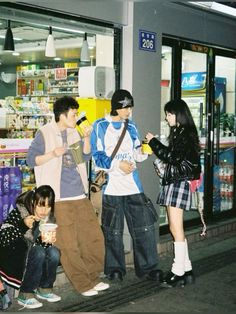 four people are standing on the sidewalk in front of a store with their cell phones