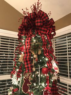 a christmas tree decorated with red, white and black plaid ribbon is in front of a window