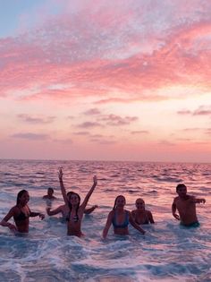 several people in the ocean at sunset with their arms up